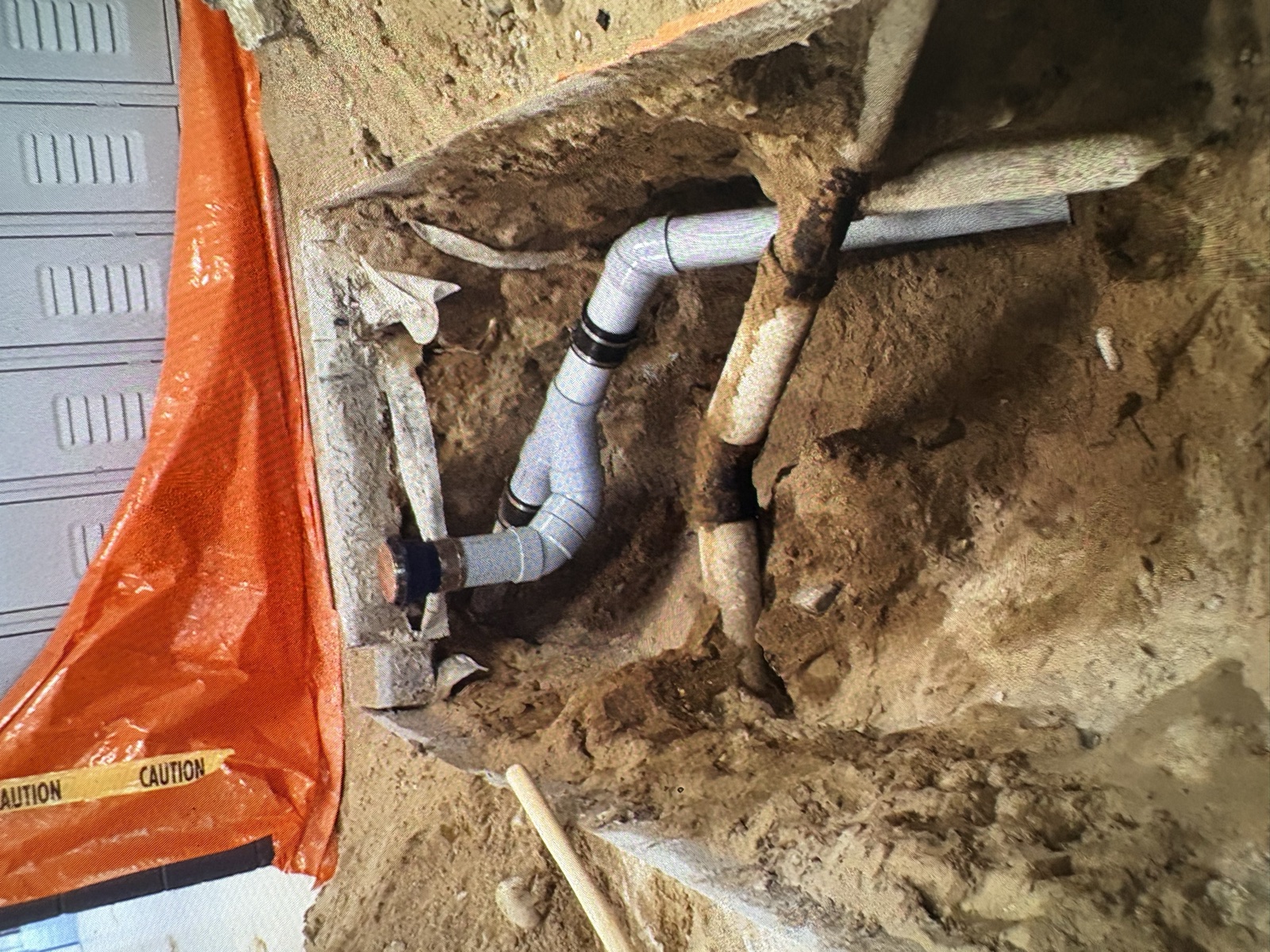 Real Thomas Plumbing job. Excavated trench showing a new PVC drain section installed beside the original cast-iron lateral on a North Bay residential repipe by Tyler Thomas.